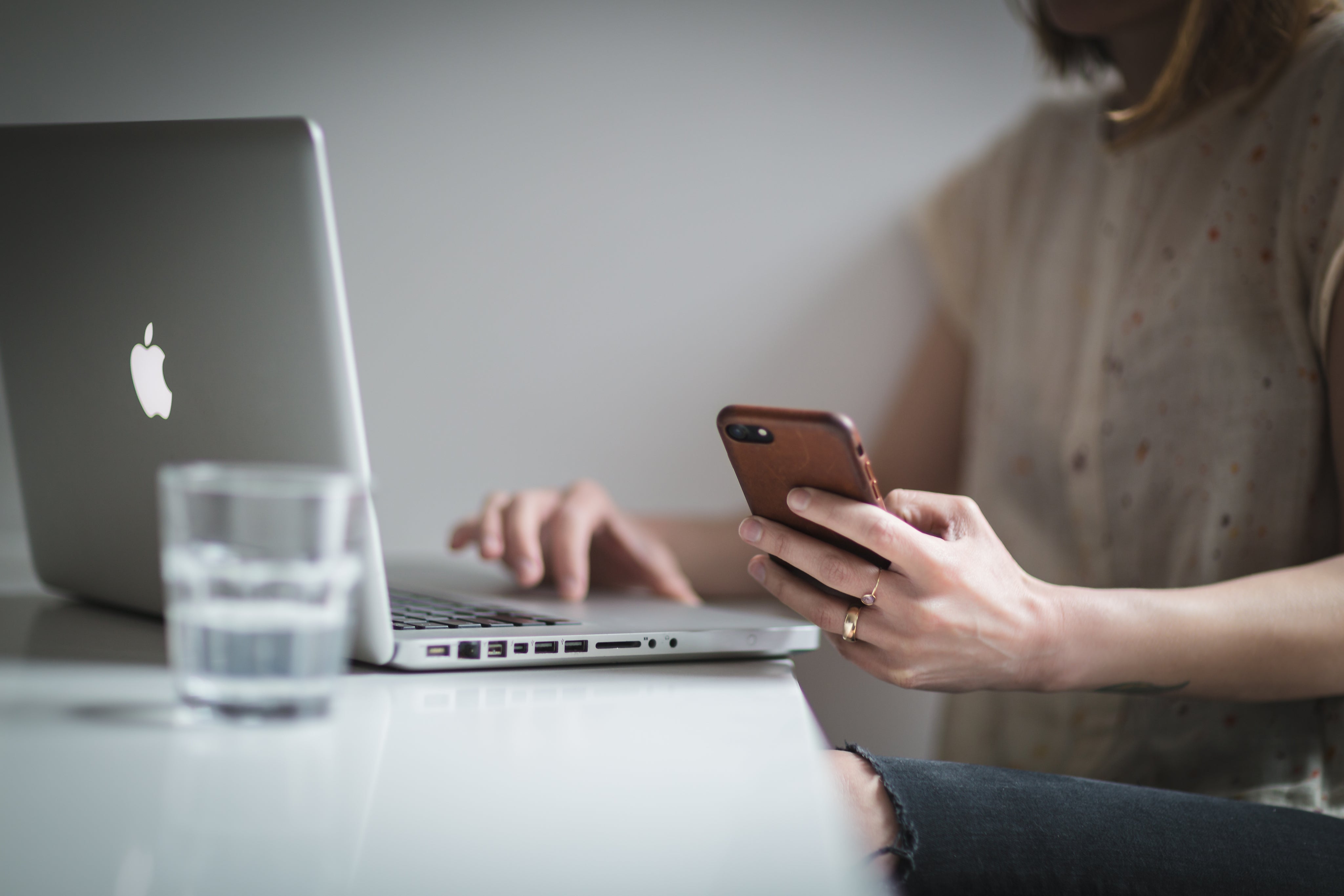 Ung kvinne sitter foran Mac-en og holder en iPhone 